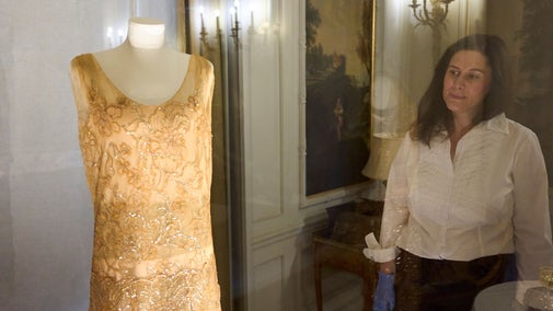 A woman looks at a dress on a mannequin in a glass case